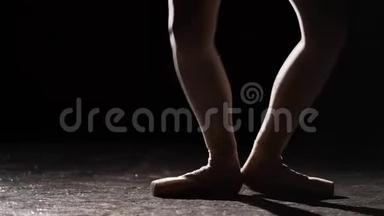 优雅的芭蕾舞演员在她的尖角芭蕾舞鞋上跳舞，在演播室的黑色背景上聚光灯下。 女孩表演经典节目